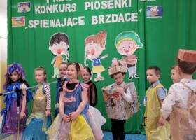 grupa dzieci w kolorowych strojach na tle zielonej dekoracji konkurs piosenki