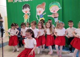 grupa dzieci w białoczerwonych strojach na tle zielonej dekoracji konkurs piosenki