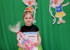 dziewczynka na tle zielonej dekoracji trzyma prezent konkurs piosenki