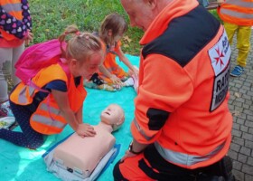 Dziewczynka ćwiczy pierwszą pomoc wykonując masaż serca na manekinie z pomocą ratownika medycznego