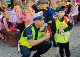 Na tle grupy policjant rozmawia do mikrofonu z chłopcem