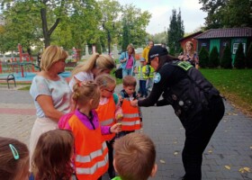 Kobieta z motocyklowej watahy rozdaje odblaski dzieciom w pomarańczowych kamizelkach