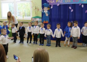 Dzieci w białych i niebieskich strojach występują z okazji pasowania na przedszkolaka